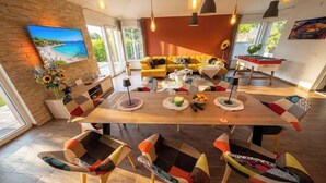 Un soggiorno moderno con un tavolo da pranzo in legno, sedie colorate, un divano e una TV a schermo piatto appesa al muro.