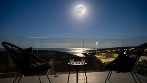 Un balcone con due sedie, un tavolino e vista sul mare e le luci della città.