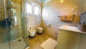 Un bagno moderno con cabina doccia in vetro, un bidet, un water, un lavandino e una finestra.