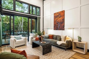A modern living room with large windows, a fireplace, and a dining area visible through the windows.