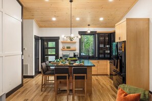 A modern kitchen with wooden cabinets, a dining table with chairs, and a large window.