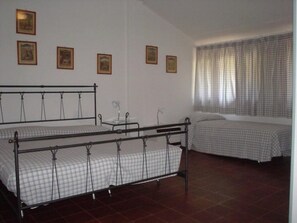 A room with two metal beds, a small table, and a window with curtains. - Spacious Stay for Families Steps From the Beach (Lignano Sabbiadoro)