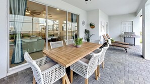 Eine Terrasse mit Holztisch, weißen Korbstühlen, einem Deckenventilator und einem Grillbereich.