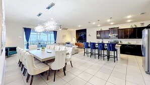 Eine moderne Küche mit dunklen Schränken, einem Edelstahlkühlschrank und einem Essbereich mit einem weißen Tisch und Stühlen.