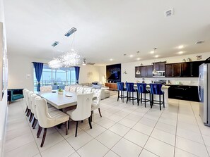 Eine moderne Küche mit dunklen Schränken, einem Edelstahlkühlschrank und einem Essbereich mit einem weißen Tisch und Stühlen.