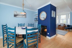 A dining area with a round table, blue chairs, a hanging light fixture, and a fireplace. - Riggers Rest Stylish Renovated Home With Parking (Cowes)