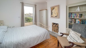 A bedroom with a bed, a chair, a bookshelf, a fireplace, and a window. - Seabreeze House Stylish 3 bed Townhouse (Cowes)