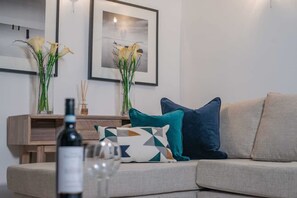Ein Wohnzimmer mit einer Couch, dekorativen Kissen, einer Weinflasche und zwei Blumenvasen.