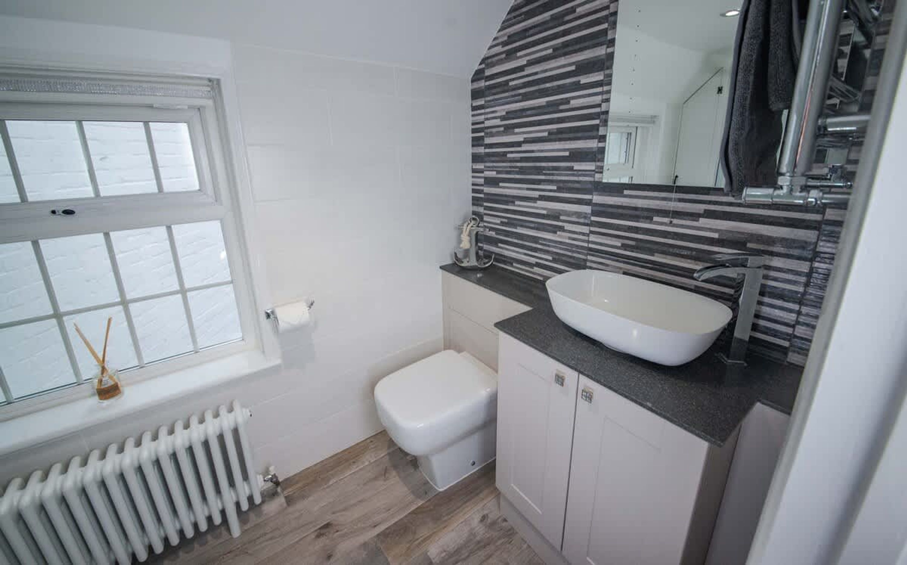 Casa de banho com sanita branca, lavatório branco, janela e radiador.