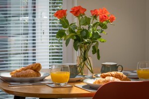 A breakfast table with croissants, orange juice, and a vase of roses. - Skysail Stylish Accessible One Bedroom Apartment (Cowes)