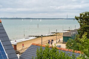 Ein Strand mit Blick auf das Meer, einige Segelboote und eine entfernte Skyline einer Stadt.
