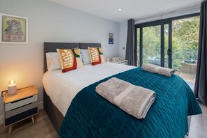 Ein Schlafzimmer mit einem großen Bett, einem Nachttisch mit Lampe und Blick auf Grün durch das Fenster.