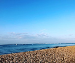 Ein Kiesstrand mit Meer und Booten in der Ferne.