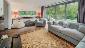 A modern living room with a sofa, ottoman, and a television. - Sandpiper House Coastal Retreat Moments From Beach (Cowes)