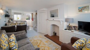 Ein Wohnzimmer mit einer Couch, einem Kamin, einem Fernseher und einer Küche im Hintergrund.