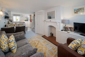 Ein Wohnzimmer mit einer Couch, einem Kamin, einem Fernseher und einer Küche im Hintergrund.