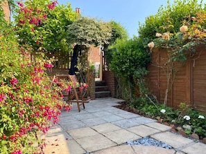 Ein Garten mit Terrassenplatten, einer Ziegelwand, einer Holzbank und verschiedenen Pflanzen.