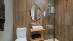 A modern bathroom with a wooden panel wall, a round mirror, a white sink, and a glass shower enclosure. - Scaw Fell Boutique Studio Annex (Cowes)