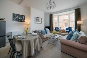 Ein Wohnzimmer mit Esstisch, Sofas, einem Chandelier und einem großen Fenster mit Blick auf ein Gebäude.