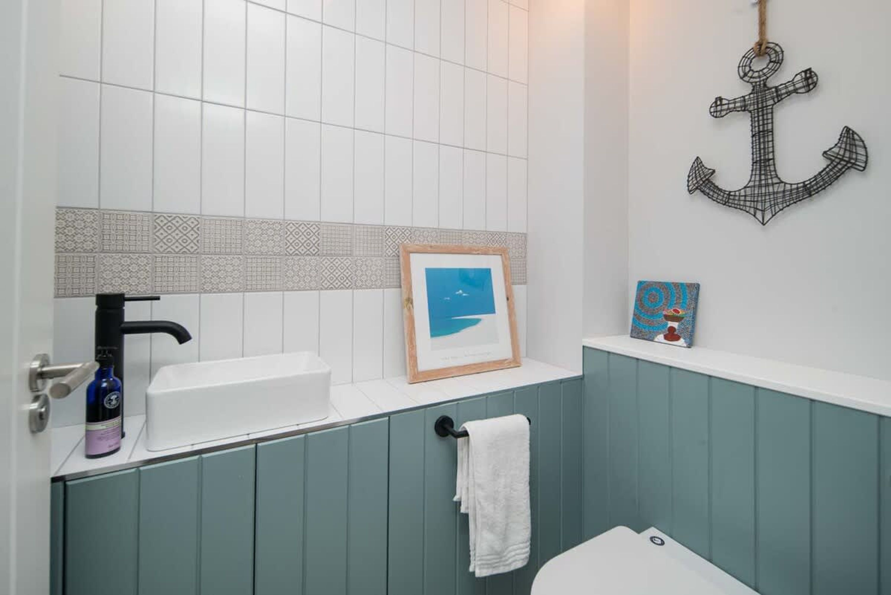 A bathroom with a white sink, a framed picture, a towel rack, and an anchor decoration.