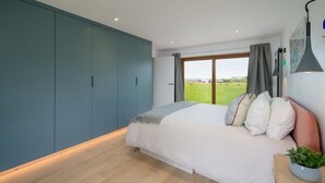 A bedroom with a bed, a large window, and a view of a green field. - Spring Hill Luxury Home Countryside Solent Views (Freshwater)