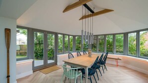 A modern dining room with a large table and chairs, large windows, and a wooden ceiling beam. - Spring Hill Luxury Home Countryside Solent Views (Freshwater)