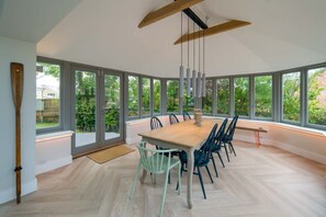 A modern dining room with a large table and chairs, large windows, and a wooden ceiling beam. - Spring Hill Luxury Home Countryside Solent Views (Freshwater)