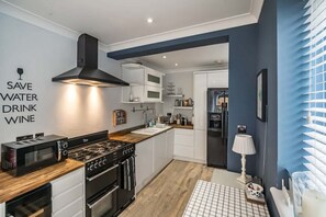 A modern kitchen with a built-in microwave, stove, and oven, white cabinetry, and a blue accent wall. - Fitzroy Central Cowes Victorian Home (Cowes)