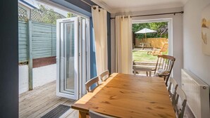 Een kamer met een houten tafel, stoelen, een schuifdeur en uitzicht op een terras met een tafel en stoelen.