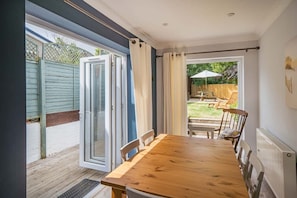 Ein Zimmer mit einem Holztisch, Stühlen, einer Schiebeglastür und Blick auf eine Terrasse mit Tisch und Stühlen.