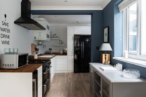 A modern kitchen with a microwave, stove, and black refrigerator. There is a window with blinds and a lamp on the counter. - Fitzroy Central Cowes Victorian Home (Cowes)