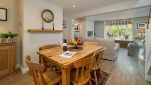 A dining area with a wooden table and chairs, a mirror on the wall, and a window with a view of greenery. - Lily Cottage Charming Gurnard Retreat by the Sea (Cowes)