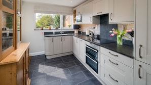 A modern kitchen with white cabinets, a black countertop, and a window with a view of greenery. - Lily Cottage Charming Gurnard Retreat by the Sea (Cowes)