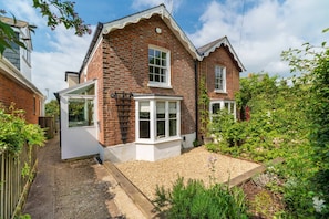 A two-story brick house with a white front door, a bay window, and a small garden area with gravel and plants. - Lily Cottage Charming Gurnard Retreat by the Sea (Cowes)