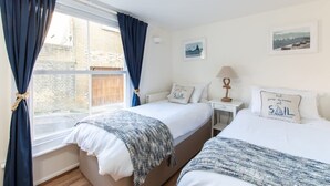 A bedroom with two beds, a window with curtains, a nightstand, a lamp, and wall art. - Bars Hill Cottage Moments From the Seafront (Cowes)