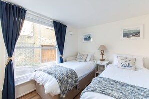 Ein Schlafzimmer mit zwei Betten, einem Fenster mit Vorhängen, einem Nachttisch, einer Lampe und Wandbildern.