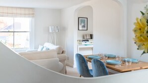 A modern living room with a sofa, a dining table set with plates and glasses, a lamp, and a framed picture on the wall. - Bars Hill Cottage Moments From the Seafront (Cowes)