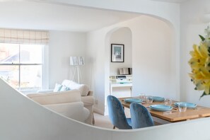 Ein modernes Wohnzimmer mit einer Couch, einem Esstisch gedeckt mit Tellern und Gläsern, einer Lampe und einem gerahmten Bild an der Wand.
