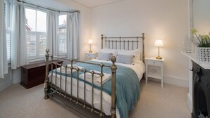 Une chambre à coucher avec un lit à cadre métallique, deux tables de chevet avec des lampes, un petit banc en bois et une cheminée.