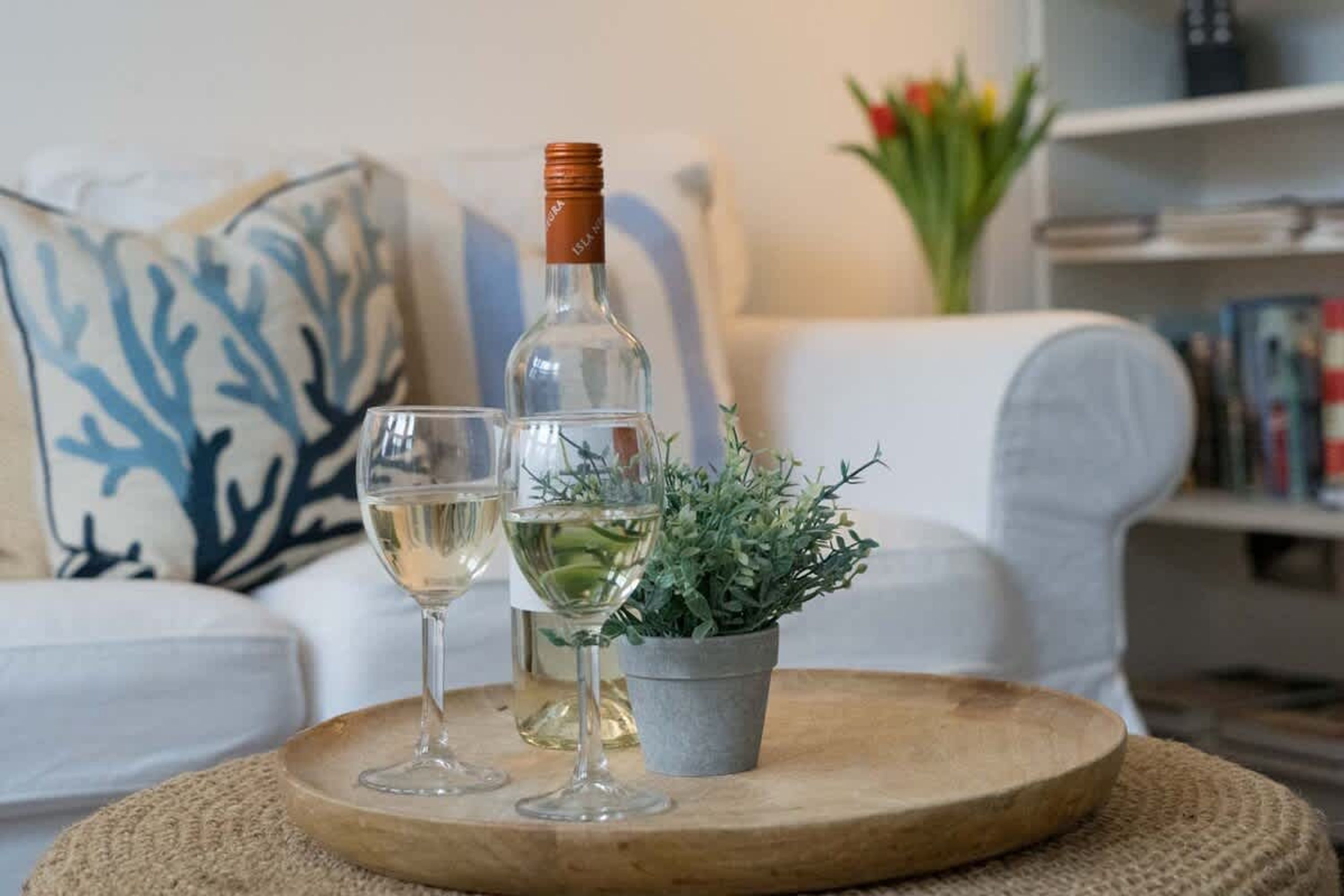 Ein hölzernes Tablett mit einer Flasche und zwei Gläsern Weißwein auf einer gewebten Matte.