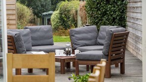 Un espace extérieur aménagé avec une terrasse en bois, des chaises rembourrées grises et une table sur laquelle se trouvent des tasses et une théière.