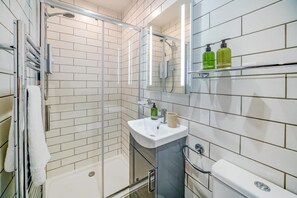 Ein modernes Badezimmer mit weißen Fliesen, einer Duschkabine aus Glas, einem Waschbecken mit Spiegel und einer Toilette.