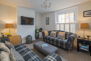 A living room with a sofa, ottoman, and a TV mounted on the wall. - Crossjack Cottage Central Cowes (Cowes)