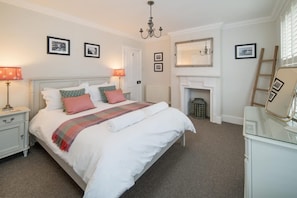 A bedroom with a bed, nightstands, a dresser, a mirror, a fireplace, and framed pictures on the walls. - Crossjack Cottage Central Cowes (Cowes)