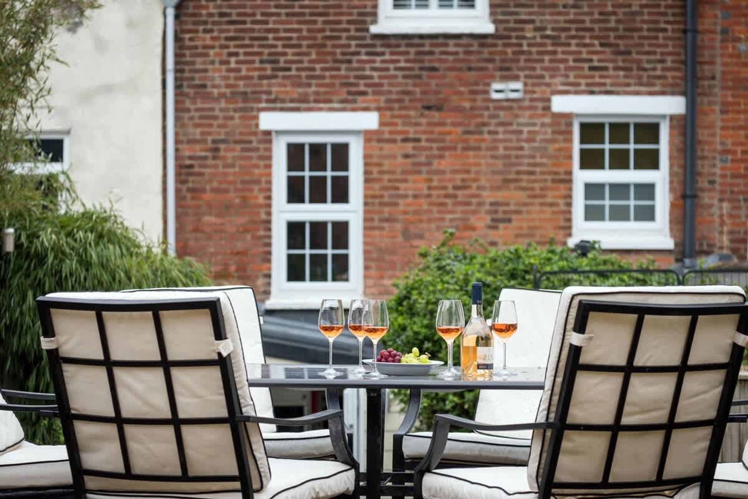 A table set for two with chairs, a glass of wine, a bottle of wine, and a bowl of fruit.