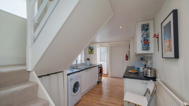 Een keuken met een wasmachine, een eetgedeelte met een stoel en een trap.