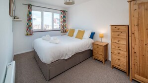 Ein Schlafzimmer mit einem Bett, Nachttischen, einem Kleiderschrank und einem Fenster mit Vorhängen.