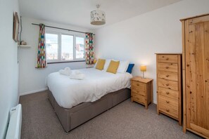 Ein Schlafzimmer mit einem Bett, Nachttischen, einem Kleiderschrank und einem Fenster mit Vorhängen.