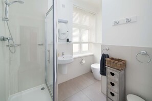 A bathroom with a glass-enclosed shower, a sink, a toilet, and a wooden storage unit. - The Chambers Apartment Central Cowes (Cowes)