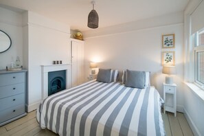 A bedroom with a bed, bedside lamps, a dresser, a fireplace, and framed pictures on the wall. - Wistaria Cottage Beautifully Renovated Cottage (Cowes)